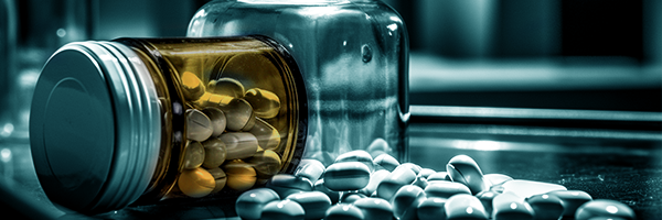 A blue-toned image of various pills and tablets in different shapes, sizes and colors on a wooden surface